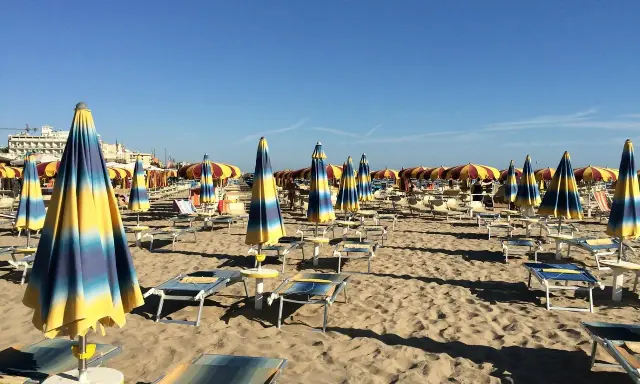 Ombrelloni a righe blu e gialle e lettini vuoti sulla spiaggia di Rivazzurra, in attesa dei bagnanti.