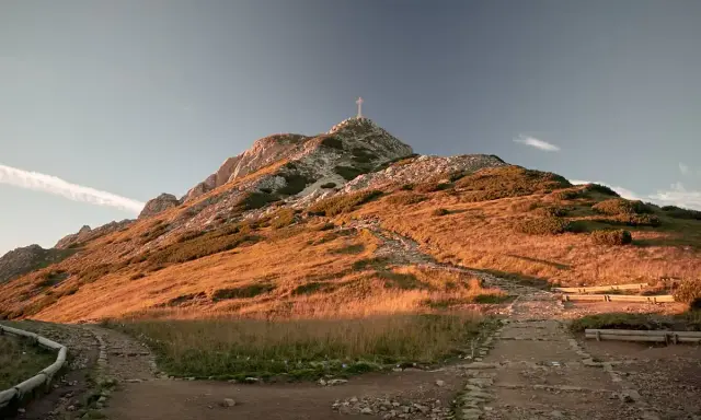 Szlak na Giewont z dzieckiem. Kamienna ścieżka wije się po zboczu oświetlonym słońcem, prowadząc ku szczytowi z krzyżem.
