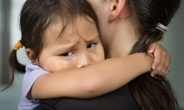 Ein Kind weint im Kindergarten und klammert sich an seine Mutter. Die Kleine hat Tränen in den Augen und sucht Trost.