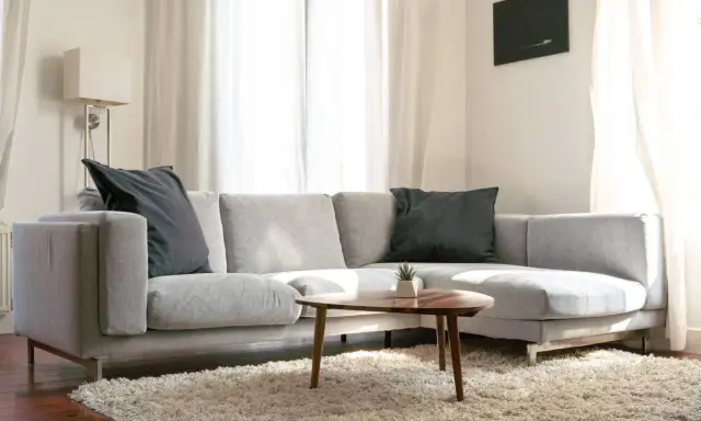 Un cómodo cheslón gris con cojines oscuros, alfombra mullida y mesa de centro de madera.
