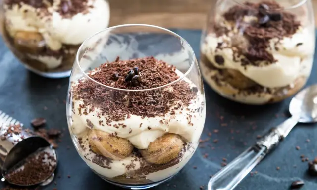 Pyszne tiramisu bez pieczenia w szklankach, udekorowane startą czekoladą i ziarnami kawy. Idealne na deser.