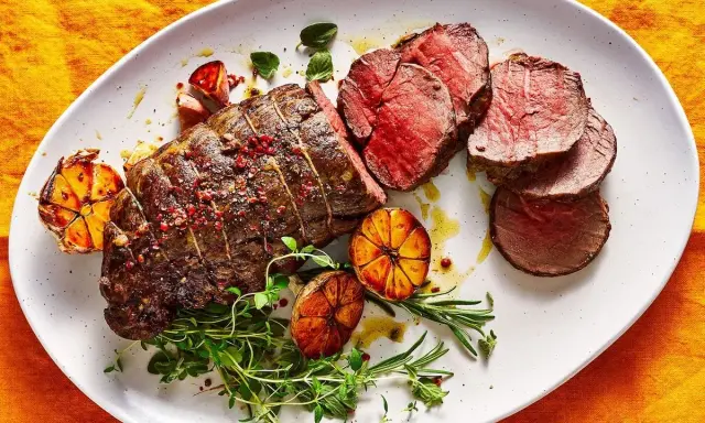 Roast beef al horno jugoso y tierno, servido con ajos asados y hierbas frescas.