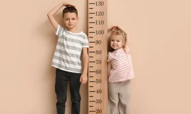 Chłopiec i dziewczynka mierzą wzrost przy drewnianej miarce. Chłopiec ma ok. 115 cm, dziewczynka ok. 85 cm. Rozmiar 68 jaki wiek?