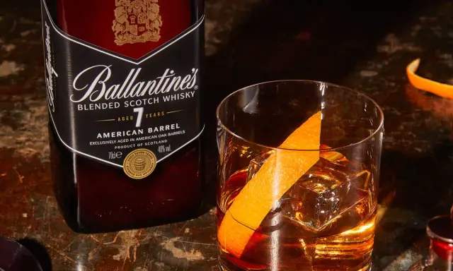 Orzeźwiający drink: whisky z wodą gazowaną, lodem i skórką pomarańczy, obok butelka Ballantine's.