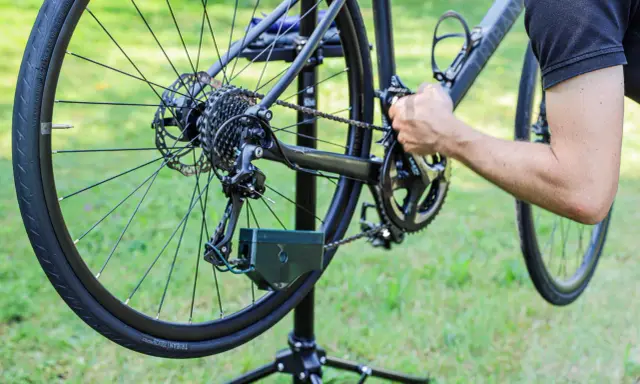Rowerzysta zakłada łańcuch w rowerze z przerzutkami. Pokazano tylną przerzutkę, kasetę i korbę.