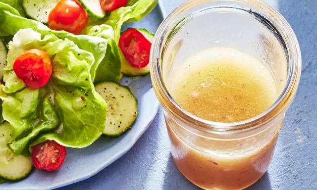 En burk med hemlagad salladsdressing bredvid en fräsch sallad med gurka och tomater. Ett perfekt salladsdressing recept för en lätt lunch.