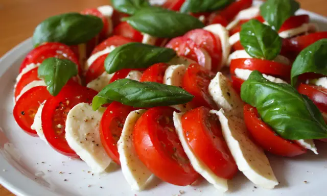 Kolorowe pomidory z mozzarellą i listkami bazylii, doprawione pieprzem, tworzą apetyczną sałatkę Caprese.