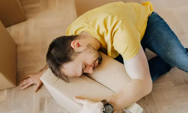Hombre agotado durmiendo sobre una caja, quizás reflexionando sobre la diferencia entre comodato y precario tras una mudanza.