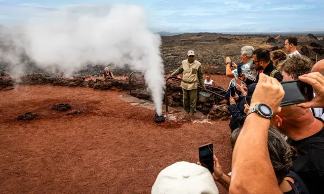 Touristen bestaunen im Nationalpark Timanfaya eine Dampf-Demonstration. Ein Führer gießt Wasser in ein Loch, das sofort zu Dampf wird.