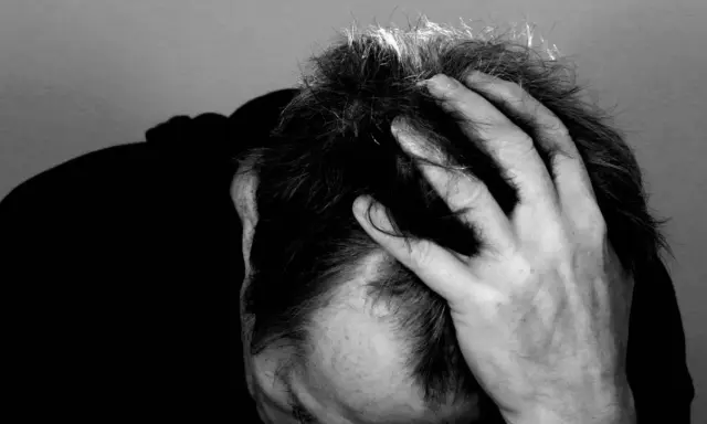Uomo con mano tra i capelli, ombra scura sul volto. Potrebbe rappresentare il peso di una diagnosi di linfoma cutaneo.