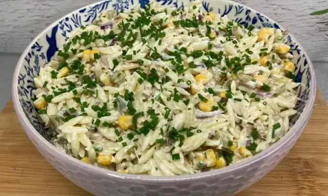 Pyszna sałatka z tuńczykiem, makaronem orzo, kukurydzą i szczypiorkiem, podana w ozdobnej misce.