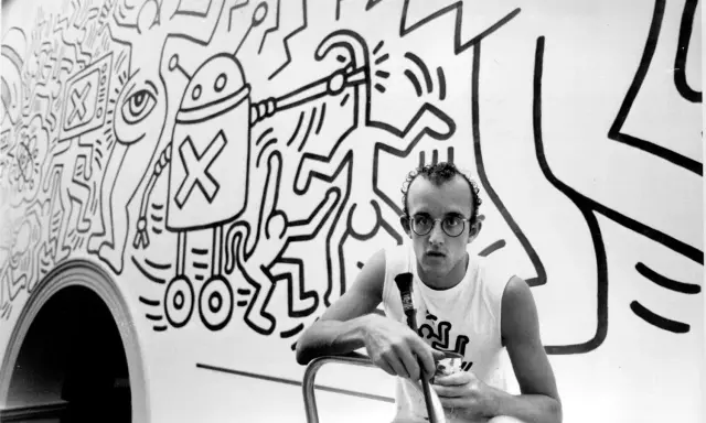 Keith Haring, a pioneer of queer art, poses with his iconic figures in this black and white image.