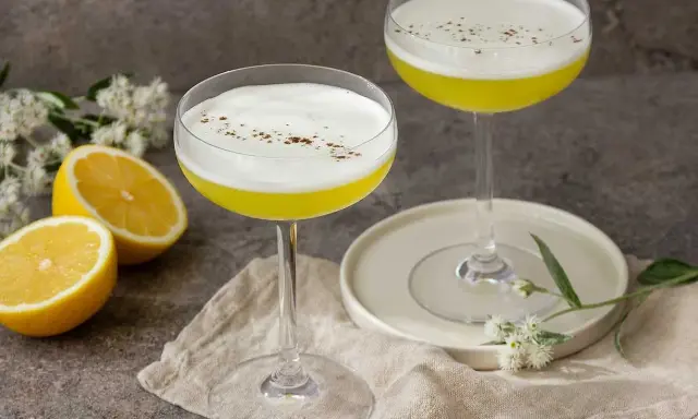 Två eleganta glas med en gul Galliano drink, toppad med vitt skum och strödd kanel. Citroner och blommor ger en fräsch touch.