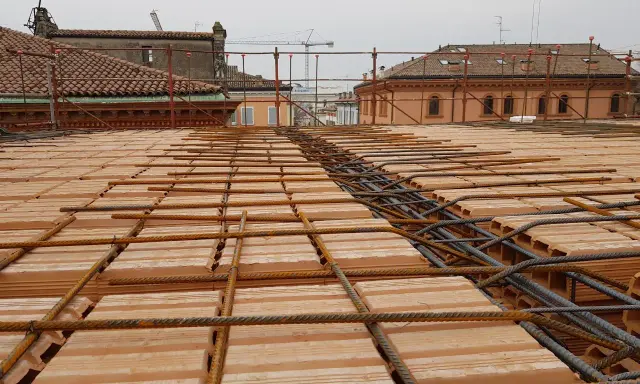 Posa di armature su tavelloni in laterizio, con sullo sfondo facciate in pietra e mattoni di edifici storici.