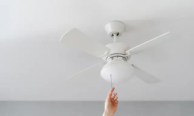 Mano tira de la cadena de un ventilador de techo pladur blanco, iluminando la habitación.