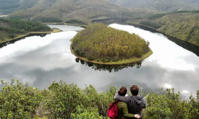 Pareja abraza contemplando el meandro del río en Las Hurdes, un paisaje de colinas verdes y agua serena.