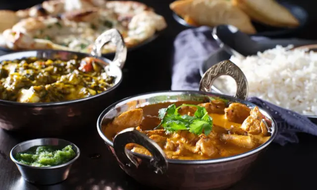 Delicioso pollo tikka masala cremoso, acompañado de arroz basmati, pan naan y una guarnición verde.
