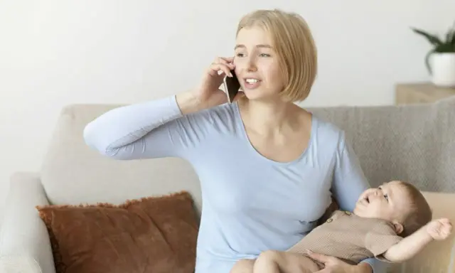 Zestresowana mama rozmawia przez telefon, trzymając dziecko, które wymiotuje po mleku modyfikowanym.