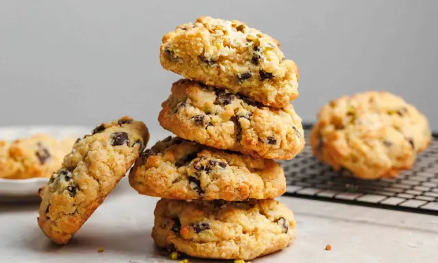 Stapel von leckeren, hausgemachten veganen Keksen mit Schokoladenstückchen und Pistazien. Ein Keks liegt daneben, ein weiterer auf einem Gitter.