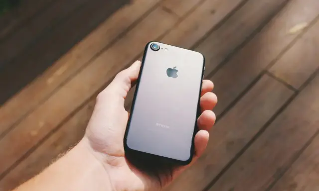 Dłoń trzyma szarego iPhone'a. Chcesz wiedzieć, jak sprawdzić, czy iPhone jest oryginalny? Zwróć uwagę na detale.