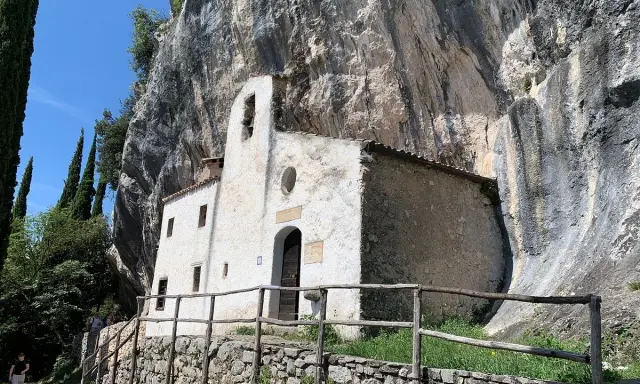 Piccolo eremo di San Valentino incastonato nella roccia, con un campanile a vela e un sentiero che conduce al suo ingresso.