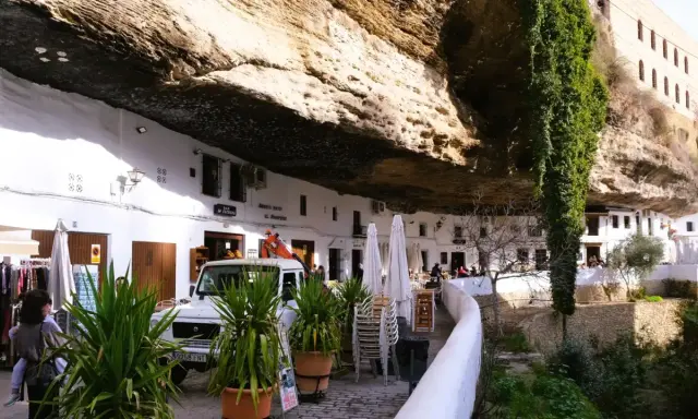 Häuser unter Felsvorsprung in Setenil de las Bodegas. Ein Auto und Pflanzen vor dem "El Gastor" Bar.