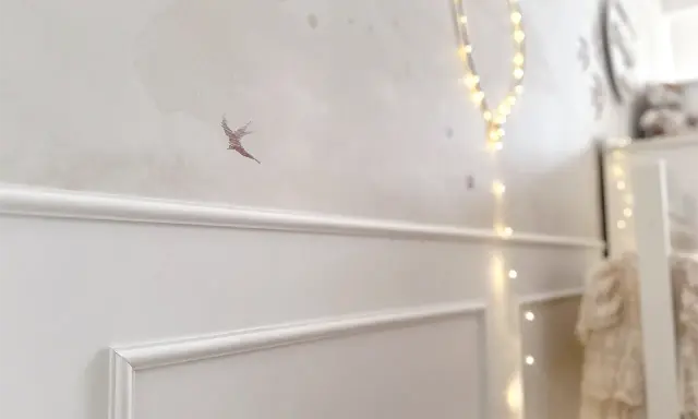 Elegancka sztukateria na ścianie w pokoju dziecka, ozdobiona motywem ptaszka i migoczącymi lampkami.