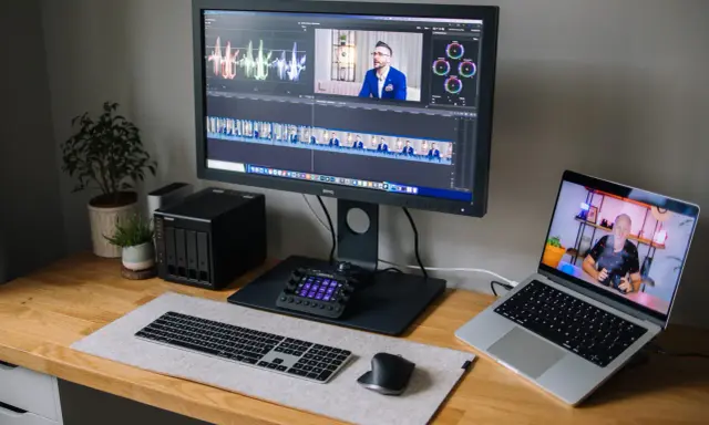 Stacja do edycji wideo z monitorem BenQ, laptopem, klawiaturą i kontrolerem. Na ekranie widać oś czasu i wykresy, co sugeruje pracę nad parametrami monitora.