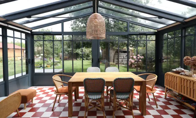 Salle à manger lumineuse dans une véranda extension, avec table en bois, chaises colorées et vue sur le jardin.