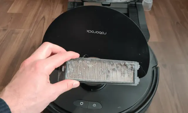 Hand hält einen stark verschmutzten Staubfilter eines Roborock Saugroboters, bereit für die Reinigung.