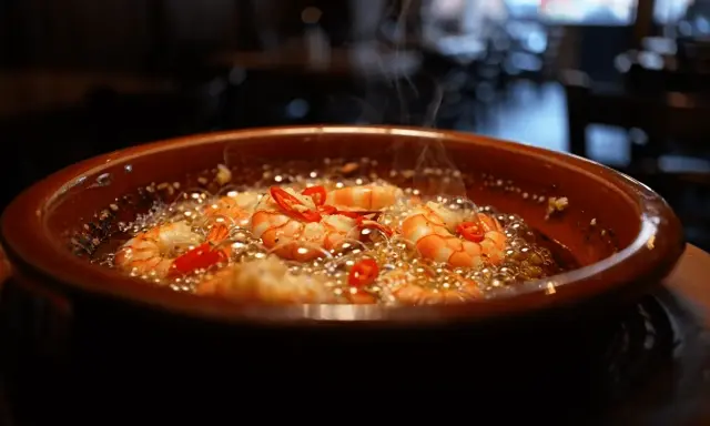 Gambas al ajillo burbujeantes en cazuela de barro, con guindillas rojas y vapor ascendiendo.