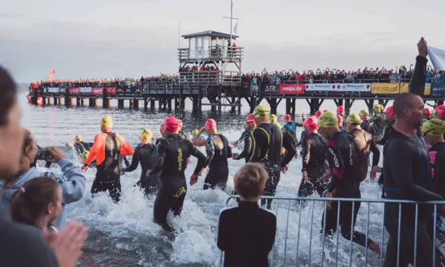 Triathleten starten ins Wasser, die Menge jubelt vom Steg. Die Ironman Vorbereitung ist in vollem Gange.