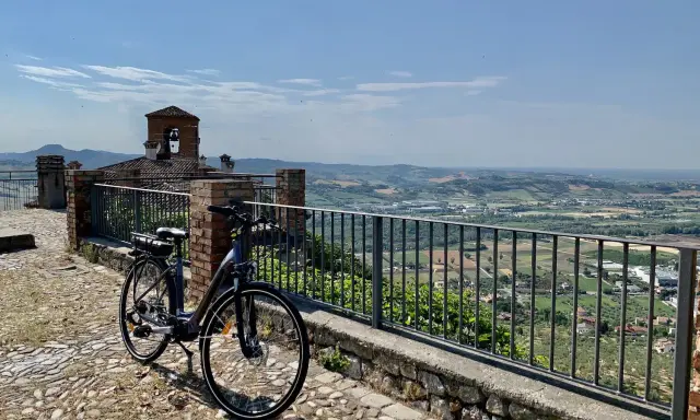 Bicicletta pronta per esplorare il **percorso fiume Marecchia**, con vista panoramica sulla valle e un antico campanile.