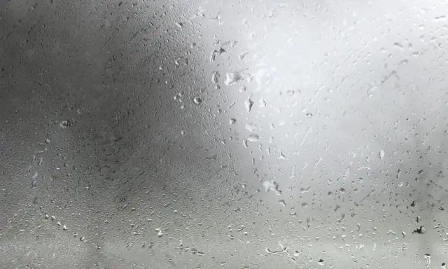Gotas de agua sobre un cristal, reflejando un cielo nublado. La **temperatura de rocío** se siente en el aire húmedo.