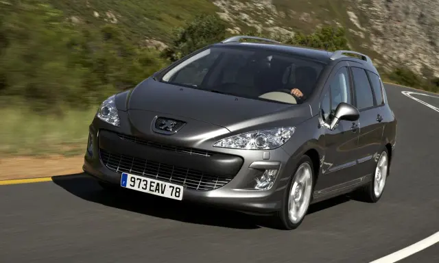 Szary Peugeot 308 2008 na krętej drodze wśród zielonych wzgórz.