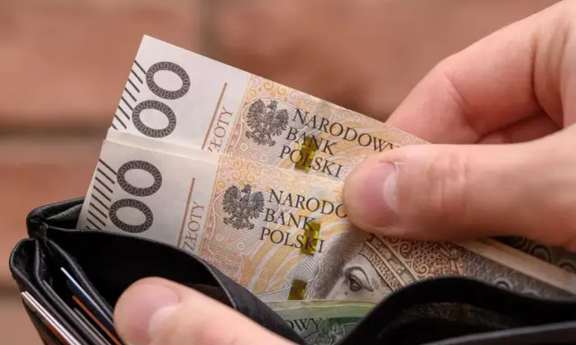 Dłoń wkłada do portfela banknoty 100 zł. Czy to na bieżące wydatki, czy może na 13. emeryturę?