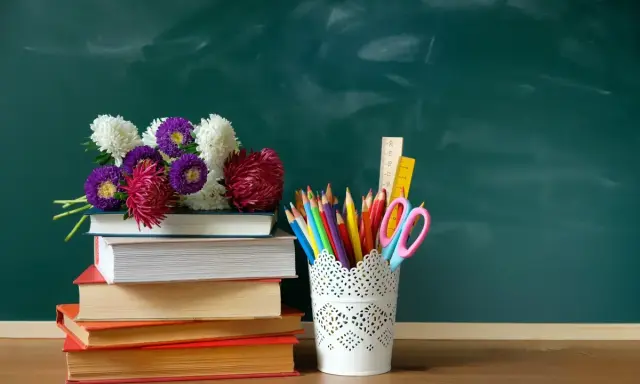 Kwiaty na stosie książek i przybory szkolne na tle zielonej tablicy. Idealna kompozycja na Dzień Edukacji Narodowej.