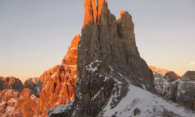 Le Torri del Vajolet illuminate dal caldo bagliore del tramonto, con la neve che ricopre le cime rocciose.