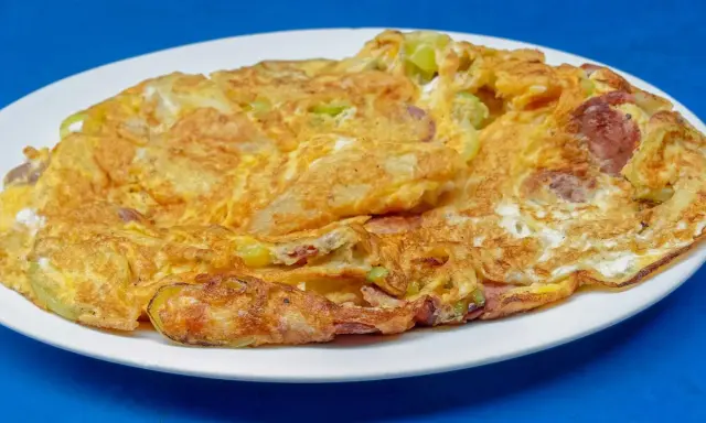 Złocisty omlet z warzywami i kawałkami kiełbasy, idealny przykład, jak się robi omlet dietetyczny.