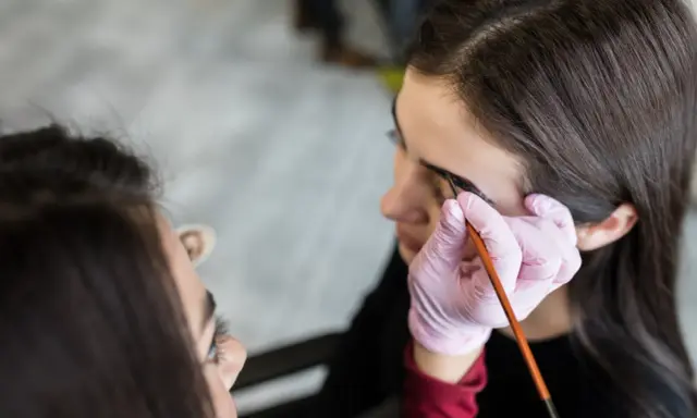 Stylistka w różowej rękawiczce aplikuje hennę pudrową na brwi klientki. Efekt naturalny, jak po hennie zwykłej, ale trwalszy.