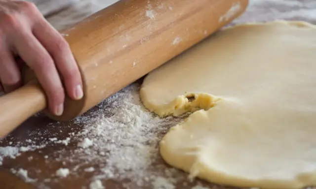 Mains roulant une pâte à biscuits trop sableux. Farine saupoudrée sur la planche en bois.