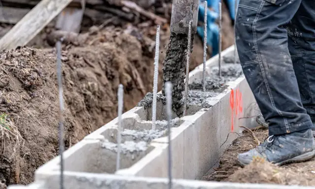 Betoniarka wylewa beton do szalunku. Pracownik w spodniach roboczych stoi obok. To kluczowy etap, by wiedzieć, jak obliczyć ilość betonu.