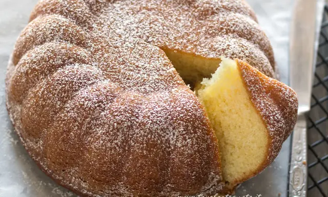Torta 7 vasetti soffice e dorata, spolverata di zucchero a velo. Una fetta è stata tagliata, rivelando l'interno profumato.