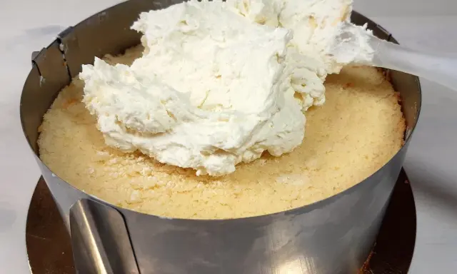 Nakładanie puszystego kremu mascarpone na biszkopt w tortownicy.