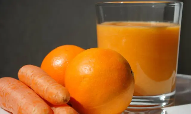 Pomarańcze i marchewki obok szklanki soku. Idealne składniki na zdrową dieta warzywno owocowa.
