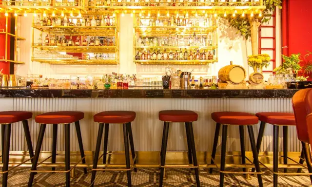 Bar con botellas doradas y taburetes rojos. Ideas para decorar un bar con poco dinero: ¡la iluminación y los detalles marcan la diferencia!