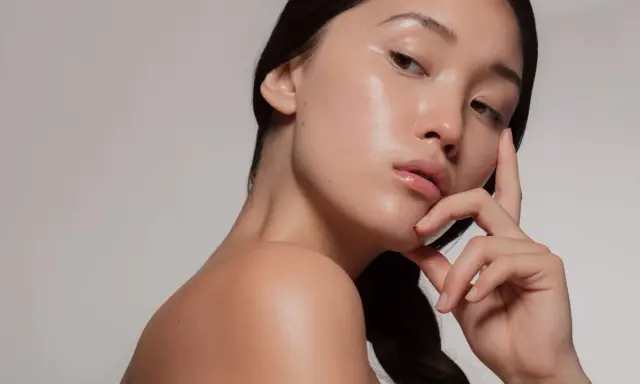 Młoda kobieta z idealną, lśniącą cerą typu "glass skin", delikatnie dotykająca twarzy.