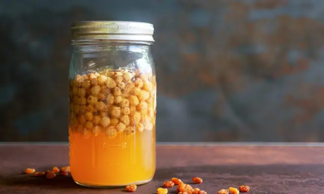 Glas mit süßem Saft und Rosinen, bereit, um Hefe selber machen zu beginnen.