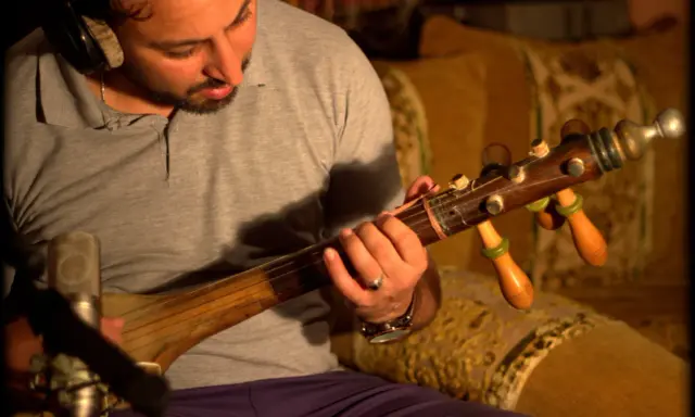 Un homme joue d'un instrument à corde marocain, un guembri, devant un microphone.