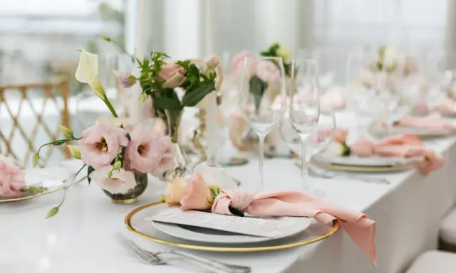 En vacker fest dukning med rosa blommor, glas och menyer.